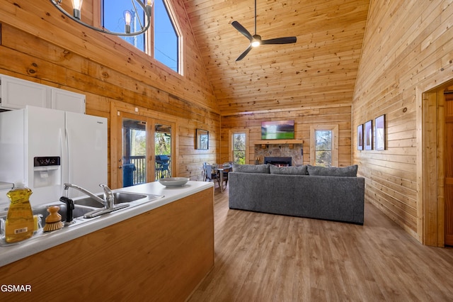 living room featuring wooden walls, ceiling fan, a fireplace, high vaulted ceiling, and light hardwood / wood-style flooring