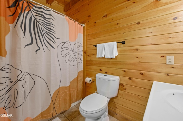 bathroom with toilet, tile patterned floors, and wood walls