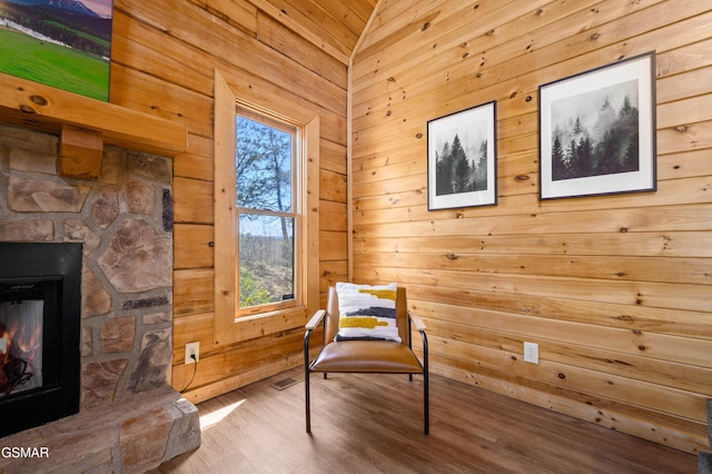 living area with wood walls, hardwood / wood-style floors, lofted ceiling, and a stone fireplace