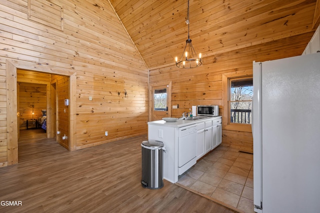 kitchen with wooden walls, white appliances, white cabinetry, hanging light fixtures, and a chandelier