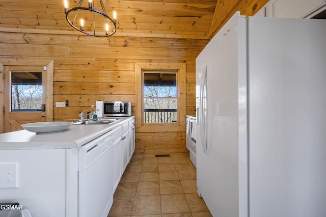 kitchen featuring light tile patterned floors, white cabinetry, wooden walls, decorative light fixtures, and white appliances