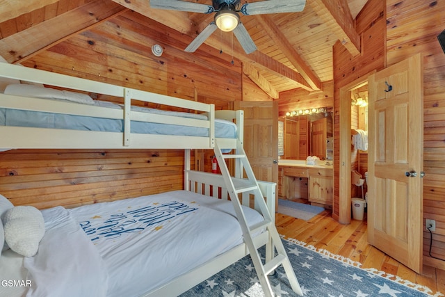 bedroom with wooden walls, lofted ceiling with beams, wood ceiling, wood-type flooring, and connected bathroom