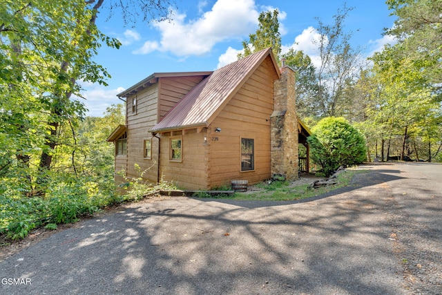 view of side of home featuring metal roof, a chimney, and aphalt driveway