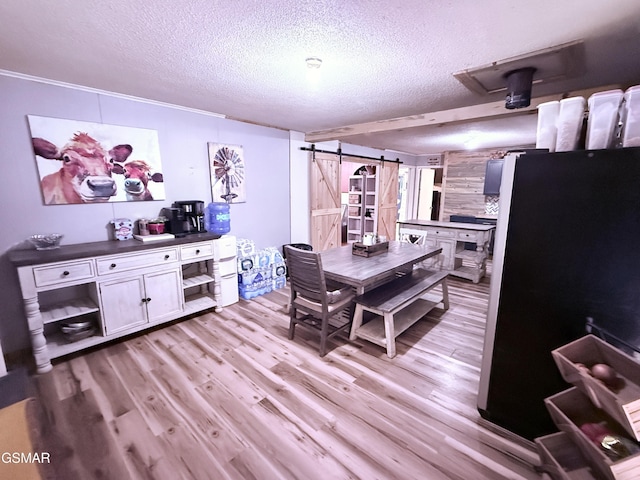 dining area featuring ornamental molding, a barn door, a textured ceiling, and light wood-type flooring