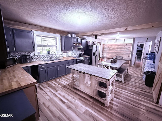 kitchen featuring butcher block countertops, sink, light hardwood / wood-style flooring, stainless steel appliances, and wall chimney exhaust hood