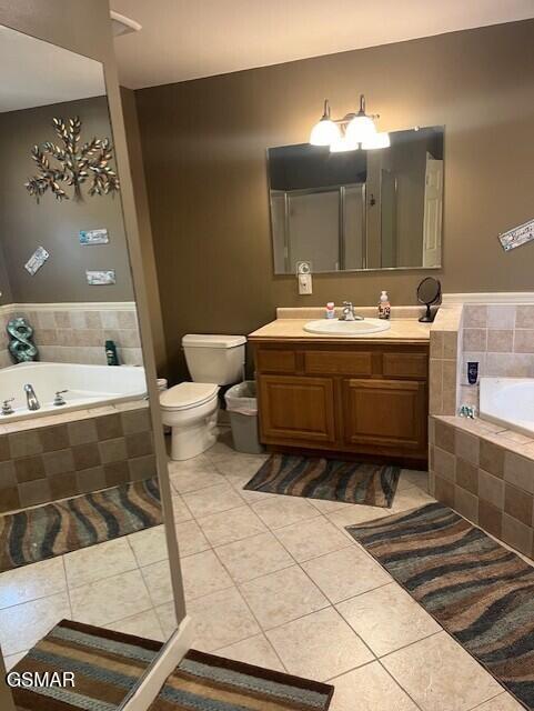 bathroom with tile patterned flooring, vanity, toilet, and tiled tub