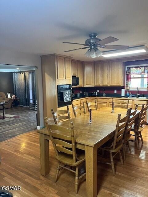 kitchen with light brown cabinetry, ceiling fan, sink, black appliances, and hardwood / wood-style floors