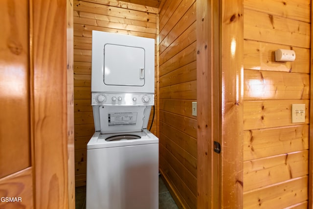 clothes washing area with laundry area, stacked washer and dryer, and wood walls