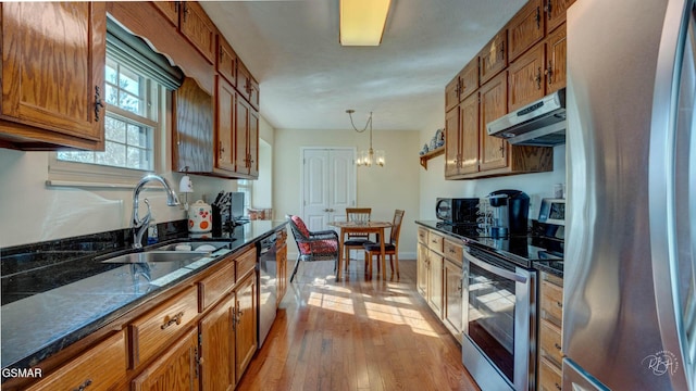 kitchen featuring appliances with stainless steel finishes, pendant lighting, sink, light wood-type flooring, and an inviting chandelier