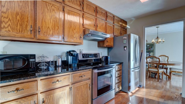 kitchen with a chandelier, dark stone counters, hanging light fixtures, light hardwood / wood-style floors, and stainless steel appliances