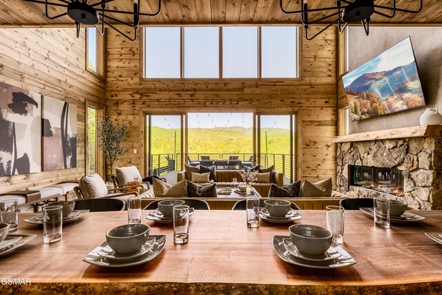 dining area with wooden ceiling, an inviting chandelier, a stone fireplace, vaulted ceiling, and wooden walls