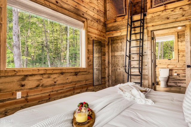 bedroom featuring ensuite bath, multiple windows, and wooden walls