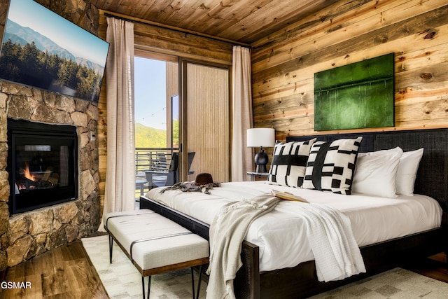 bedroom featuring wood ceiling, wood finished floors, access to exterior, a stone fireplace, and wood walls