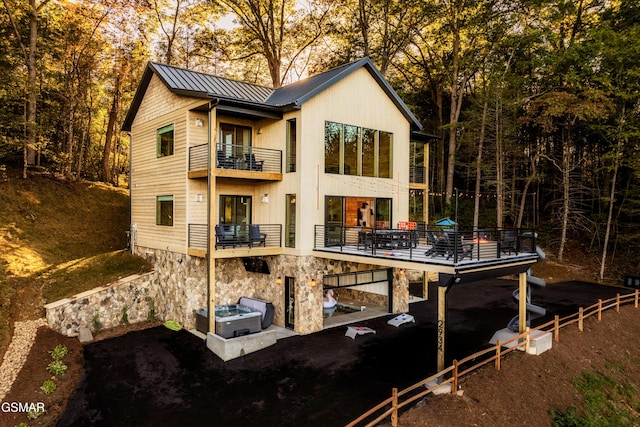 back of property featuring central air condition unit, a standing seam roof, metal roof, a balcony, and stone siding