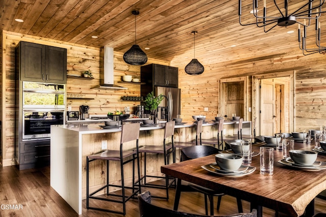 kitchen featuring dark brown cabinetry, wooden ceiling, wooden walls, a breakfast bar, and exhaust hood