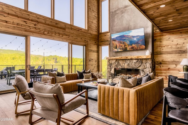 living room featuring wooden walls, recessed lighting, a stone fireplace, and wood finished floors