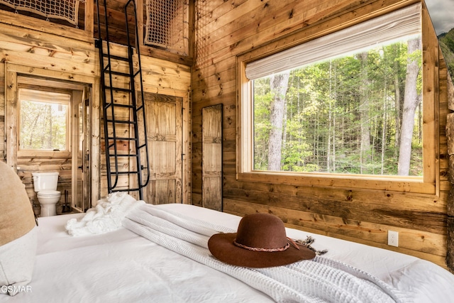 bedroom with ensuite bathroom, wooden walls, and multiple windows