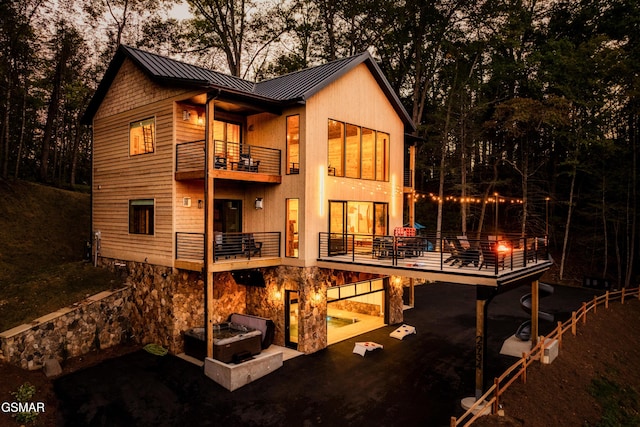 back of house at dusk with a patio, a standing seam roof, metal roof, a balcony, and stone siding