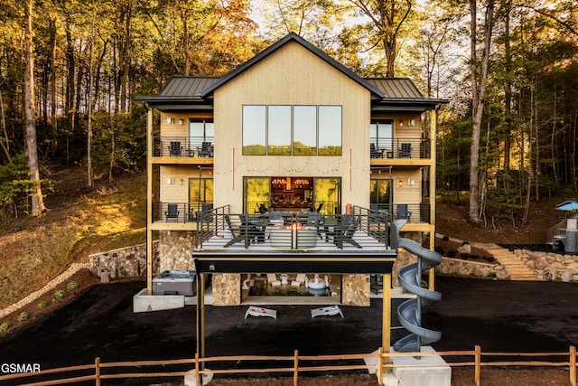 rear view of house featuring a balcony, a standing seam roof, and a fenced front yard