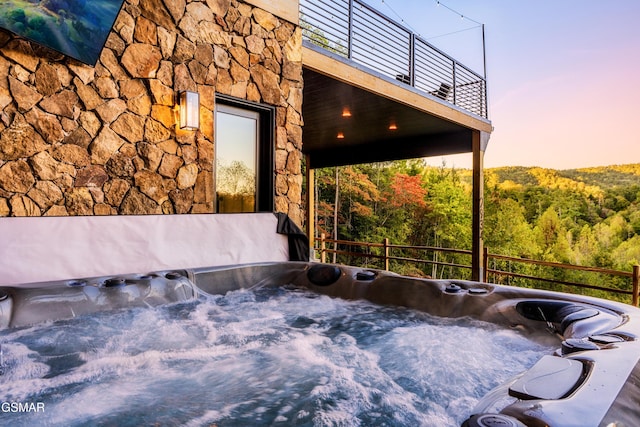 view of patio featuring a balcony, a hot tub, and a wooded view