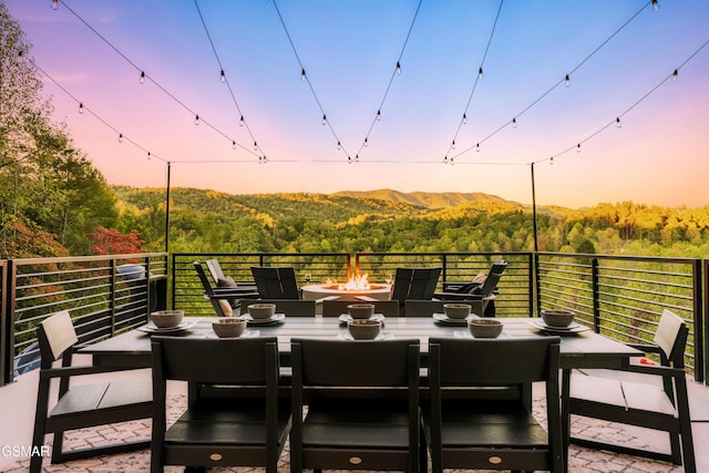 patio terrace at dusk with a fire pit, a forest view, outdoor dining space, and a mountain view