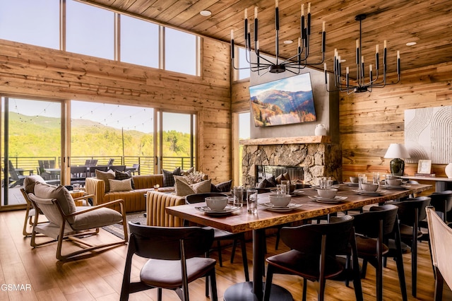 dining area with wooden ceiling, wood-type flooring, a stone fireplace, wood walls, and a chandelier