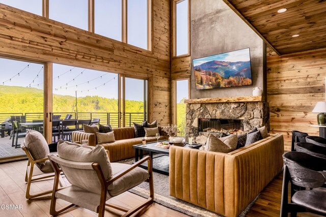 living room featuring a stone fireplace, a towering ceiling, wood-type flooring, and wooden walls