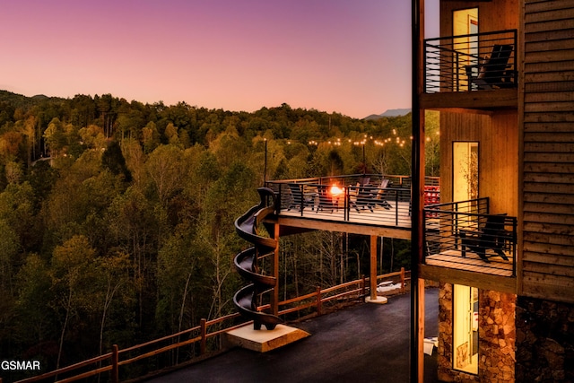 balcony at dusk featuring a view of trees