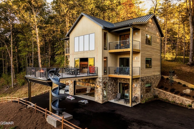 rear view of property with a patio, a balcony, stone siding, metal roof, and a standing seam roof