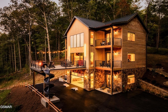 exterior space featuring metal roof, a patio, a balcony, stone siding, and a standing seam roof