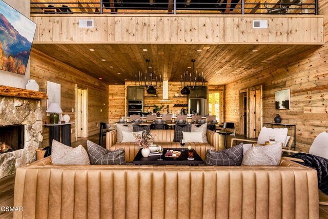 living area with wooden walls, visible vents, wood ceiling, wood finished floors, and a stone fireplace