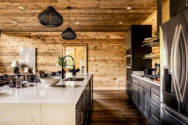 kitchen featuring wood walls, sink, pendant lighting, and appliances with stainless steel finishes