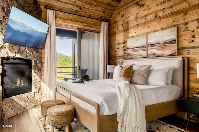 bedroom featuring a stone fireplace, wooden walls, wood finished floors, access to exterior, and vaulted ceiling