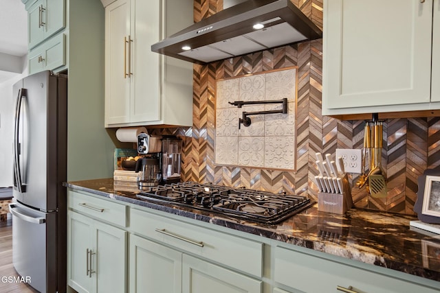 kitchen with black gas cooktop, tasteful backsplash, freestanding refrigerator, wall chimney range hood, and dark stone counters