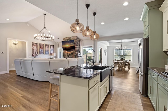 kitchen featuring decorative light fixtures, a center island with sink, stainless steel appliances, open floor plan, and green cabinetry