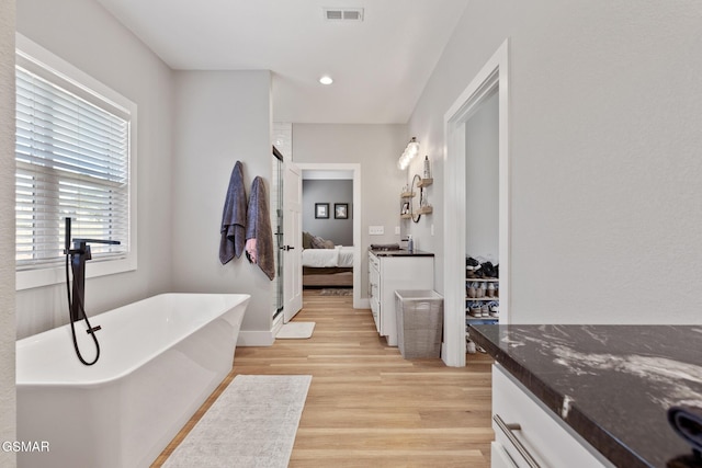 ensuite bathroom with visible vents, ensuite bath, wood finished floors, a freestanding bath, and vanity