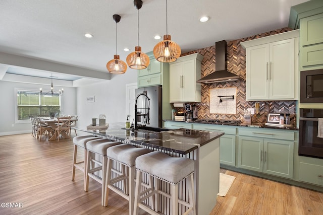 kitchen featuring hanging light fixtures, black appliances, wall chimney exhaust hood, and a kitchen island with sink