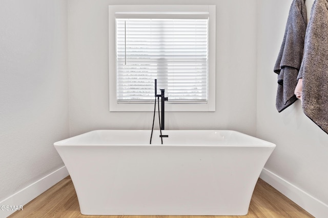 full bath with a soaking tub, wood finished floors, and baseboards