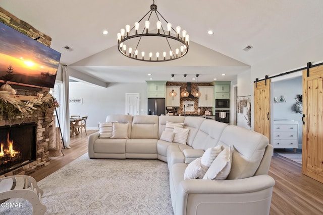 living area with light wood finished floors, lofted ceiling, visible vents, a barn door, and a stone fireplace