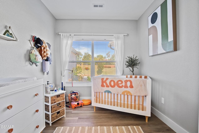 bedroom featuring a crib, baseboards, visible vents, and wood finished floors