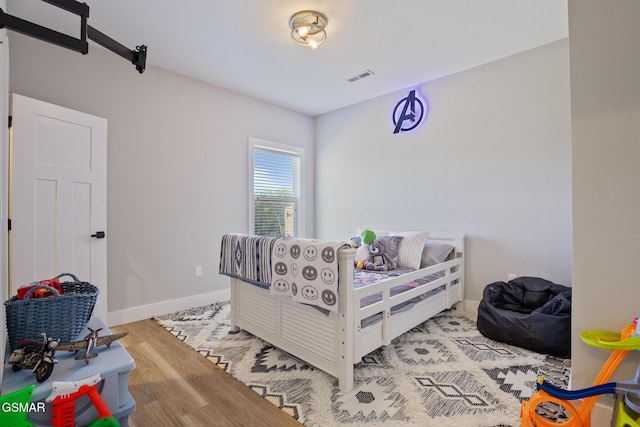 bedroom with light wood finished floors, visible vents, and baseboards