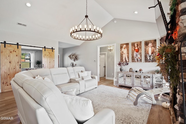 living room featuring wood finished floors, visible vents, vaulted ceiling, and a barn door