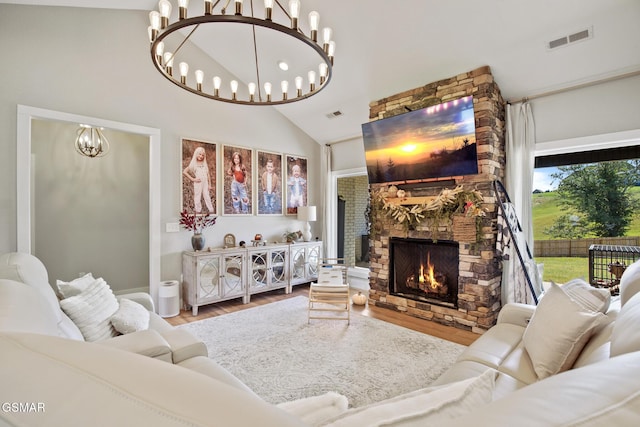 living room with visible vents, an inviting chandelier, vaulted ceiling, a stone fireplace, and light wood-type flooring