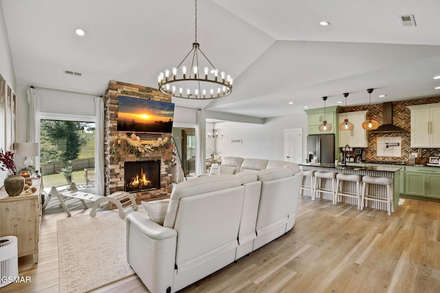 living area with vaulted ceiling, light wood-style flooring, a fireplace, and visible vents