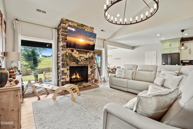 living room with vaulted ceiling, a stone fireplace, light wood-style flooring, and visible vents