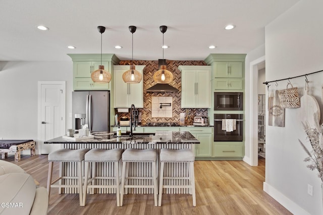 kitchen with wall chimney exhaust hood, green cabinetry, hanging light fixtures, and black appliances