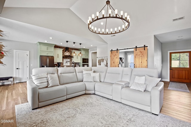 living area featuring light wood-style floors, a barn door, visible vents, and high vaulted ceiling