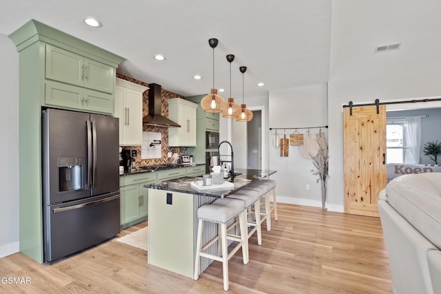 kitchen featuring a barn door, appliances with stainless steel finishes, a breakfast bar area, wall chimney range hood, and pendant lighting