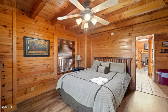 bedroom featuring beam ceiling, wood-type flooring, wooden ceiling, wooden walls, and a fireplace