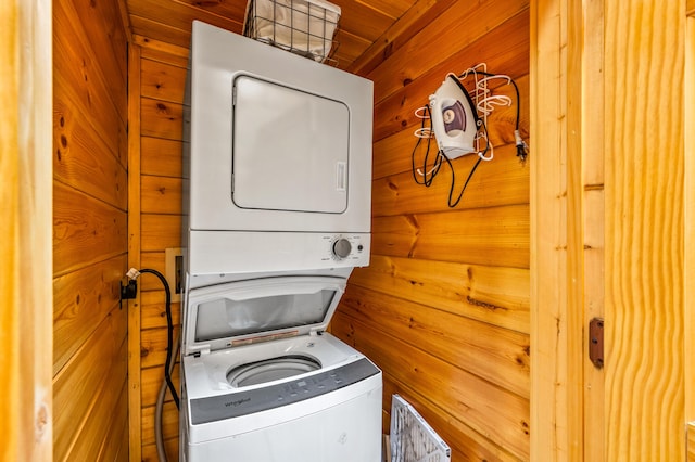 clothes washing area featuring stacked washer / drying machine and wooden walls